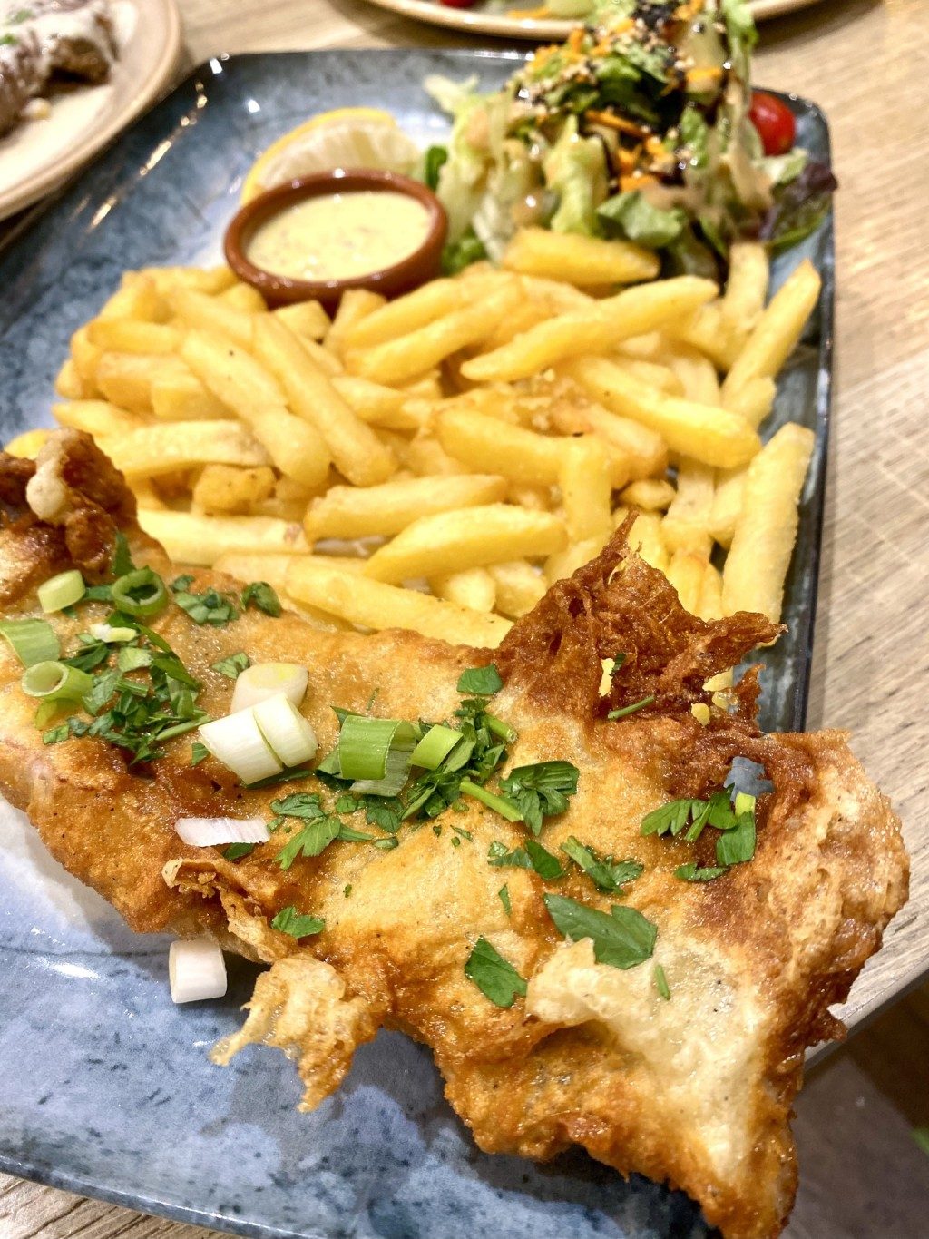 Un poisson pané doré, frites, oignons nouveaux et sauce, sur un plat bleu