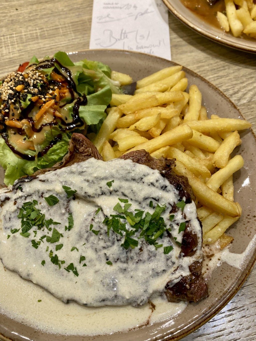 Un steak nappé de sauce crémeuse aux herbes, avec frites et salade